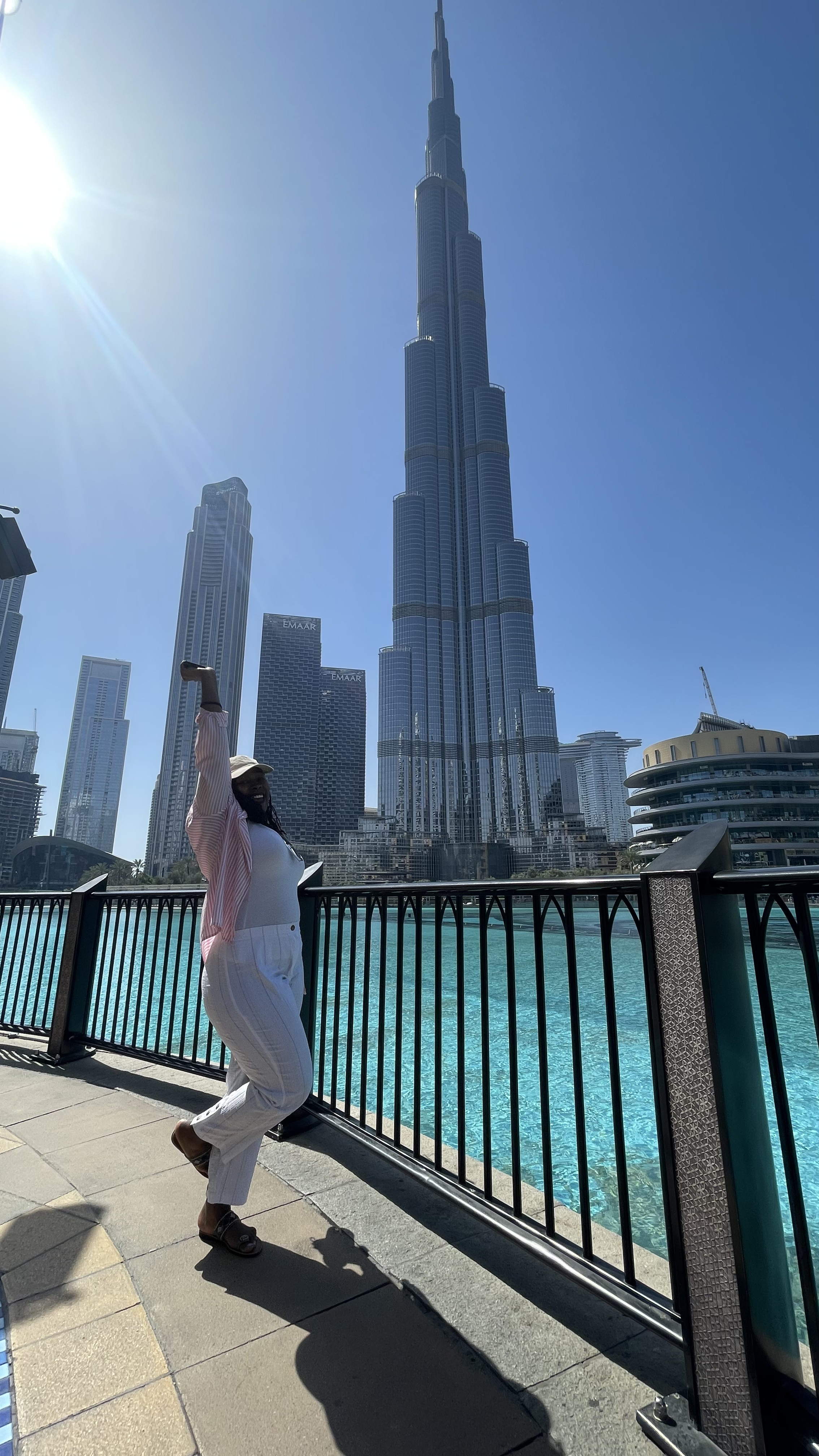 Liz on the waterfront in downtown Dubai with one arm raised, the Burj Khalifa behind her.